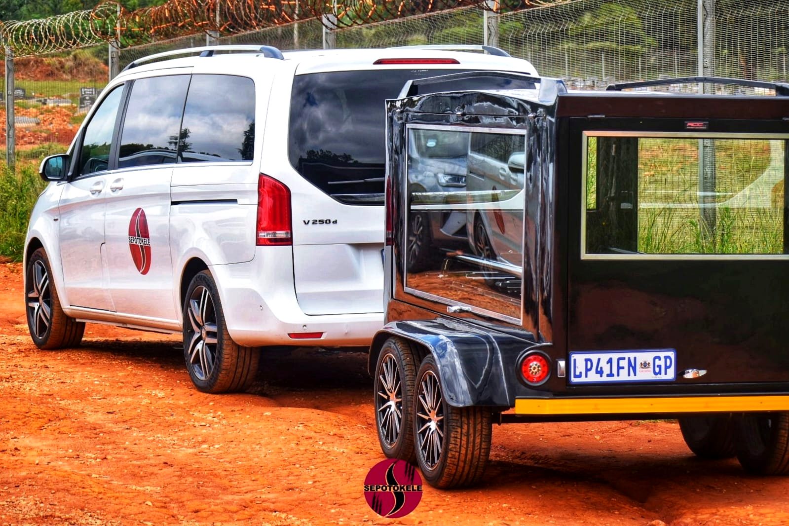 White Mercedes-Benz V250d towing the Sepotokele glass hearse trailer at a cemetery